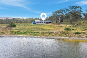 A modern building with a glass facade, situated on a grassy field with a body of water in the foreground.