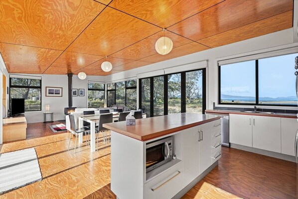 A modern kitchen with a central island, large windows, and a view of the outdoors.