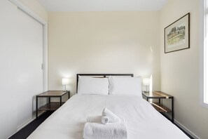 A hotel room with a bed, two bedside tables, a nightstand, a framed picture on the wall, and a window.