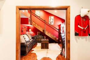 Une pièce avec un escalier en bois, un canapé en cuir, une table basse en bois et un uniforme rouge accroché au mur.