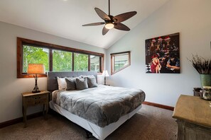 Une chambre à coucher avec un lit, deux tables de chevet, un ventilateur de plafond et une fenêtre donnant sur des arbres.