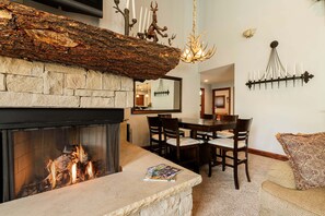 A stone fireplace with a fire, a dining area with chairs, a chandelier, and wall-mounted candles. - Spacious 4BR Deer Valley condo with 3.5 baths, ideal for 12 guests. (Park City)