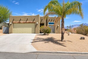 A single-story house with a garage, a small garden with a palm tree, and a desert landscape in the background. - Mountain View Santa Fe Villa with Private Spa, Heated Pool by Joshua Tree (Desert Hot Springs)