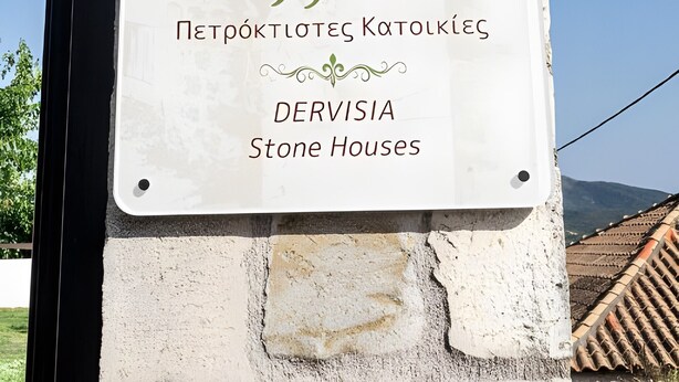 Une enseigne pour « Dervisia Stone Houses », avec une illustration représentant une maison en pierre.
