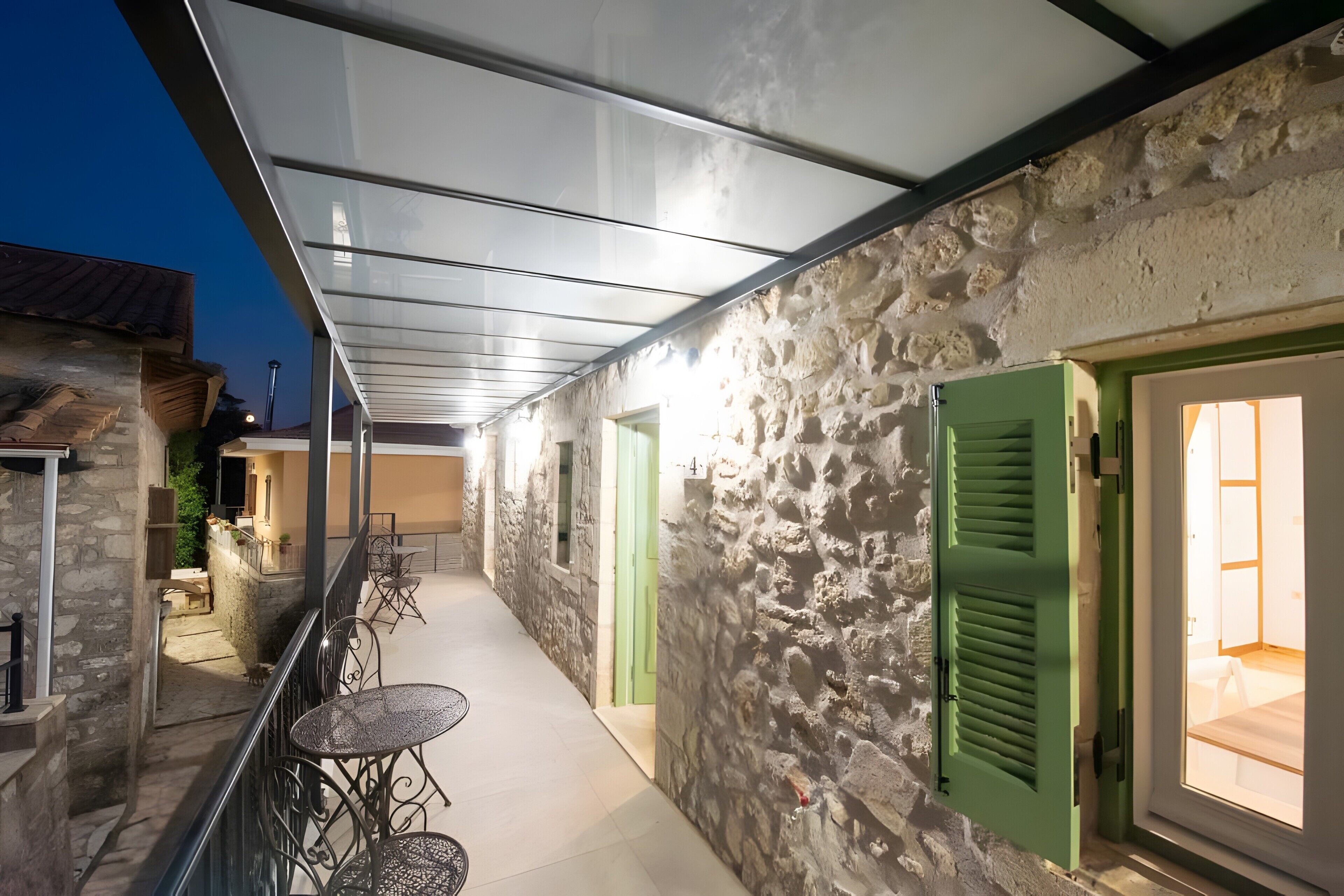 A corridor with stone walls, green doors, and outdoor seating.