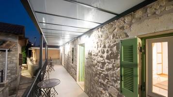 A corridor with stone walls, green doors, and outdoor seating.