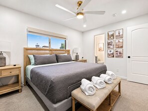 A bedroom with a large bed, a ceiling fan, a window with a view, a bench with towels, and a door with framed pictures. - Old Town 5 Min, Heated Pool & Spa & Putting Green (Scottsdale)