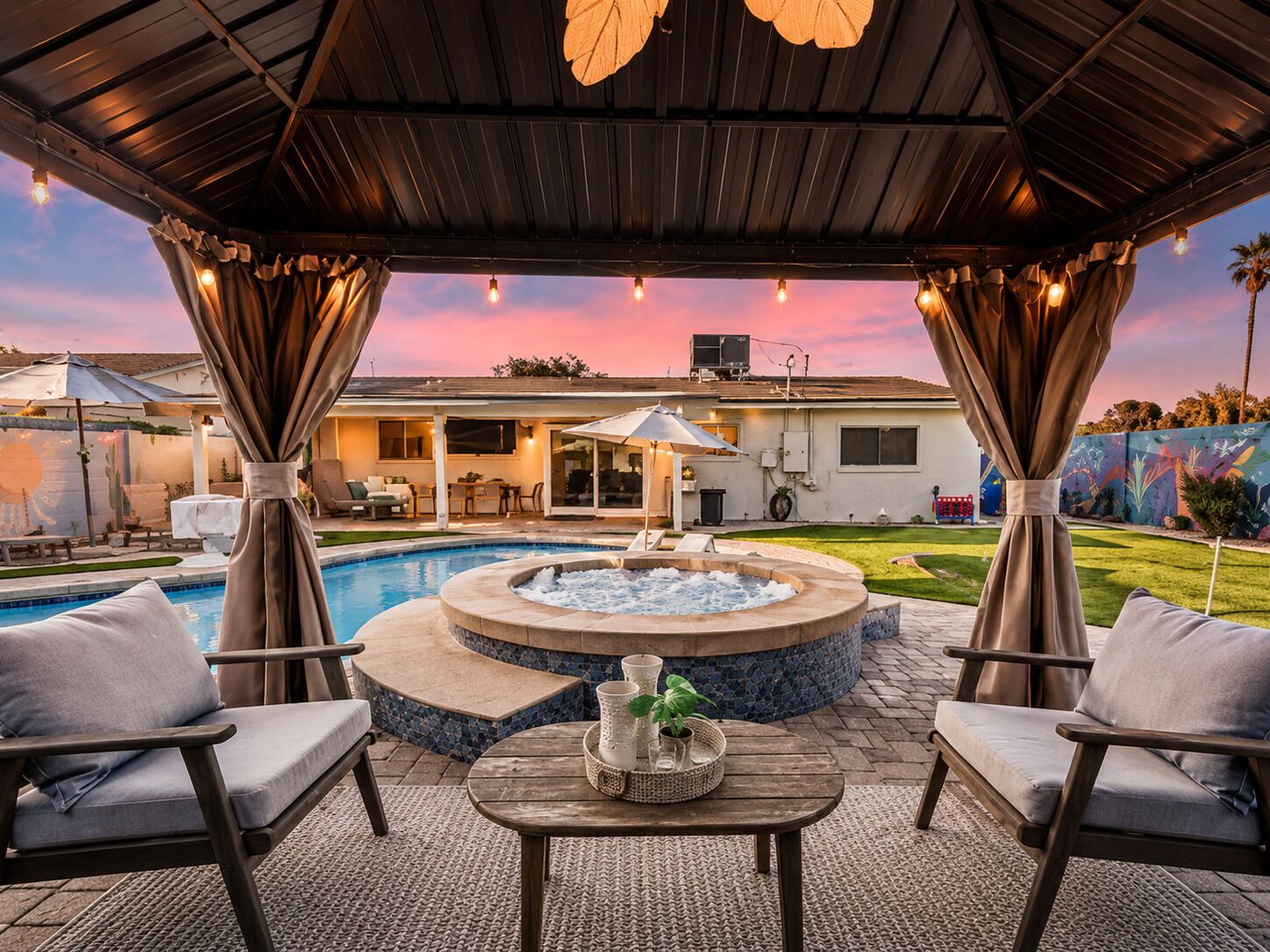 An outdoor patio with a hot tub, seating, and a view of a house.