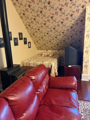 Ein Zimmer mit einem roten Ledersofa, einem Bett mit Blumenmuster an der Wand, einem schwarzen Heizgerät und einem Fernseher.