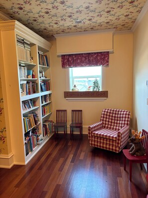 Ein gemütliches Zimmer mit Bücherregal, zwei Stühlen, einem karierten Sessel und einem Fenster mit Blick.