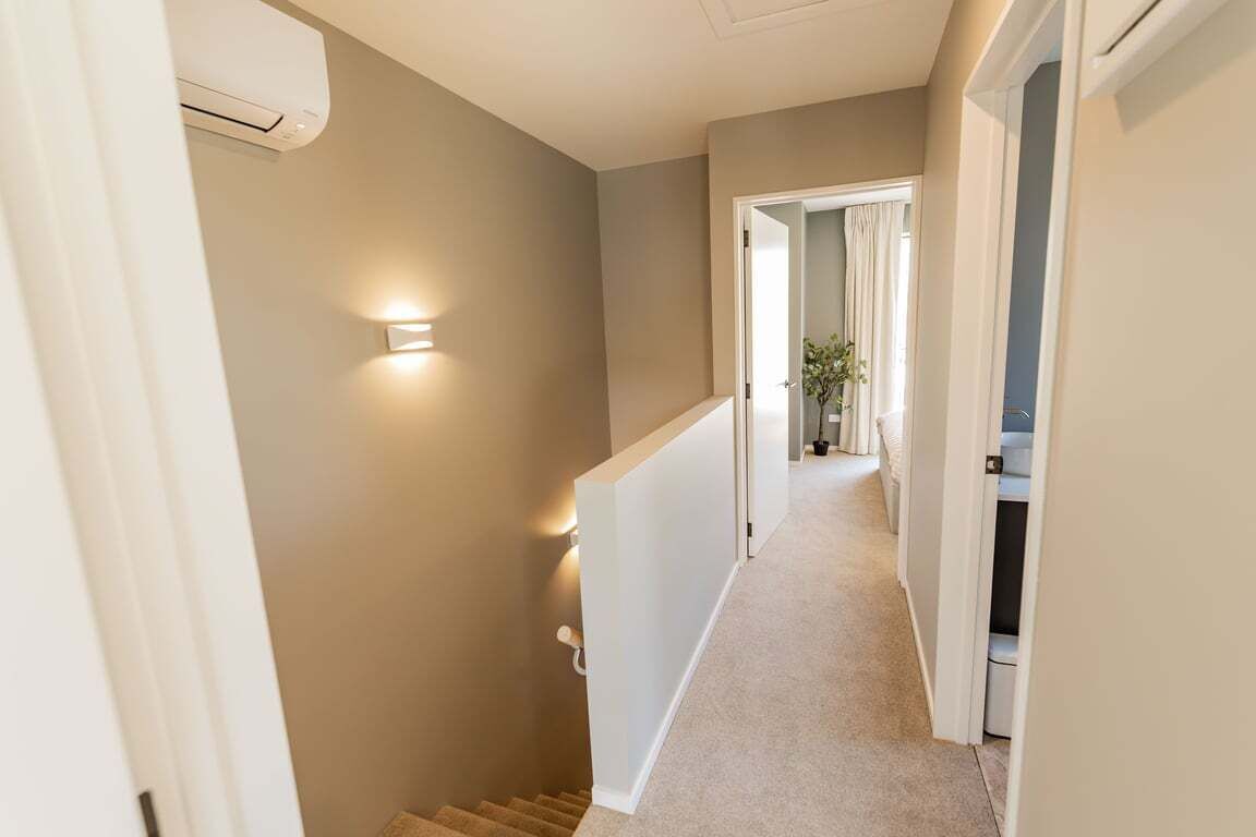 A narrow hallway with a carpeted floor, a staircase, and a door leading to another room.