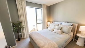 Ein modernes Schlafzimmer mit einem großen Bett, einer Topfpflanze und Blick durch eine Schiebetür.