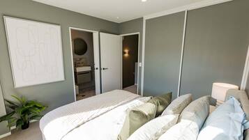 Ein Schlafzimmer mit einem Bett, Kissen, einer Nachttischlampe, einer Topfpflanze und einer Tür zu einem Badezimmer.