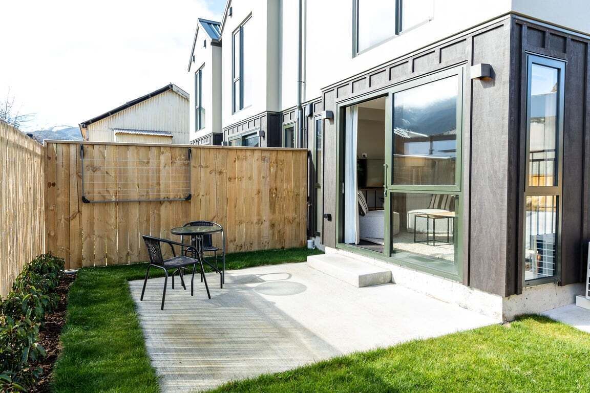 A modern house with a patio, a wooden fence, and a glass door leading to a room.