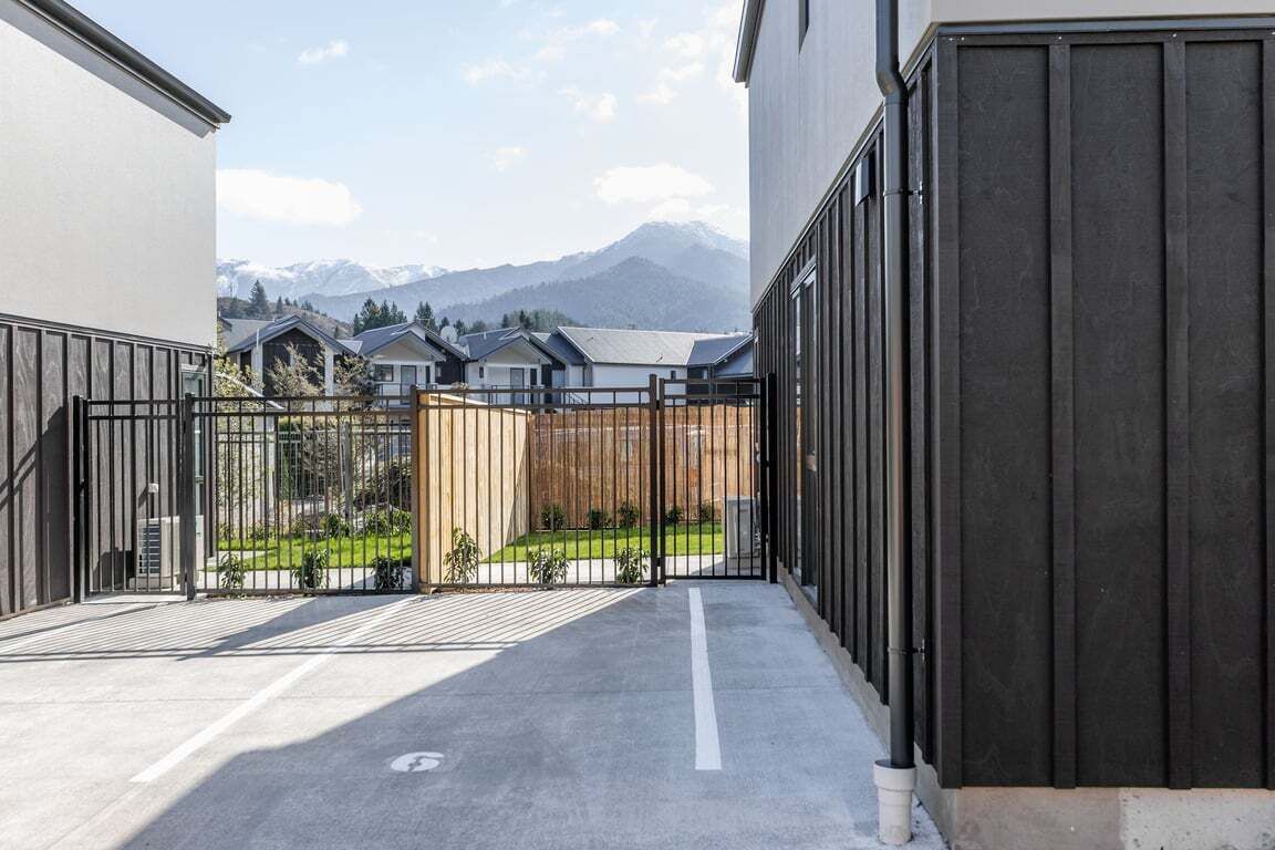 A gated courtyard with a view of mountains, a paved walkway, and a building with a dark facade.