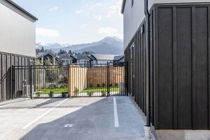 A gated courtyard with a view of mountains, a paved walkway, and a building with a dark facade.