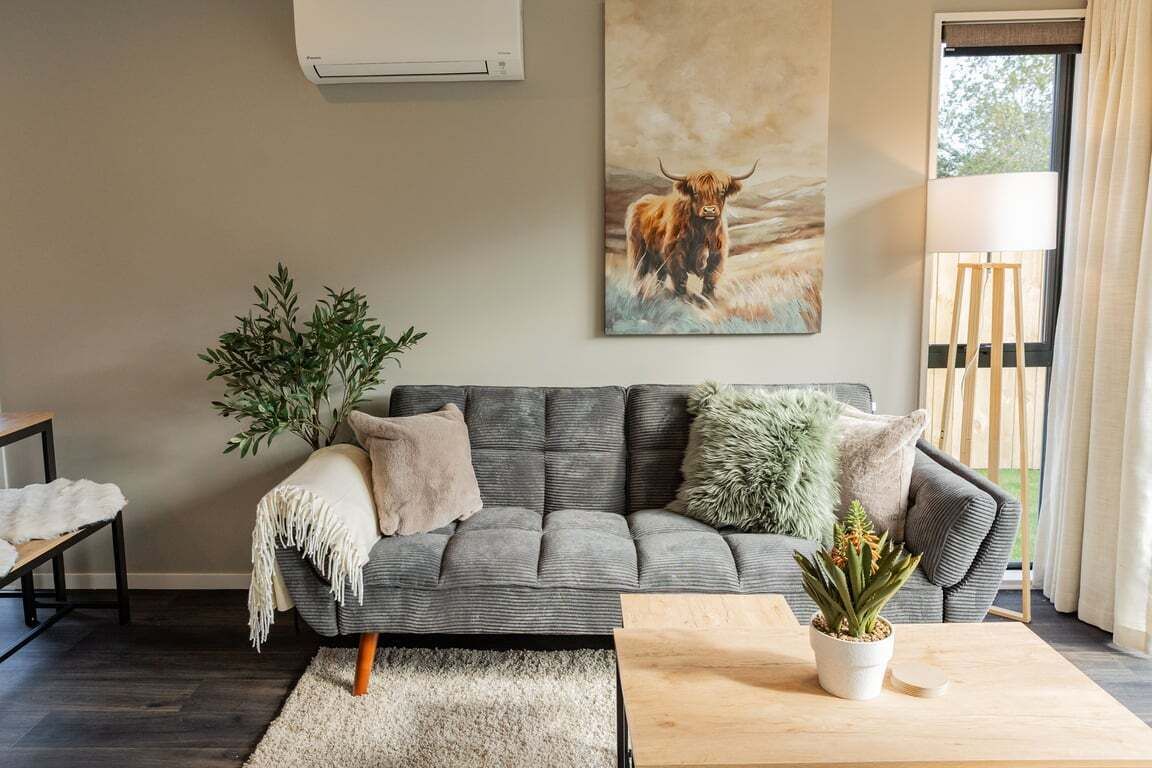 A living room with a grey sofa, a coffee table, a potted plant, and a painting of a bull on the wall.
