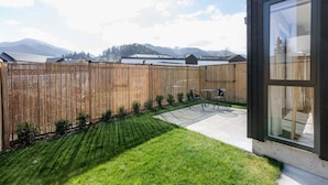Ein Garten mit Holzzaun, Rasen und einer Terrasse mit Tisch und Stühlen.
