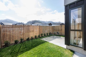 A backyard with a wooden fence, a lawn, and a patio area with a table and chairs. - Prime Location | Modern Comfort | Pools Close - HS6926 (Hanmer Springs)