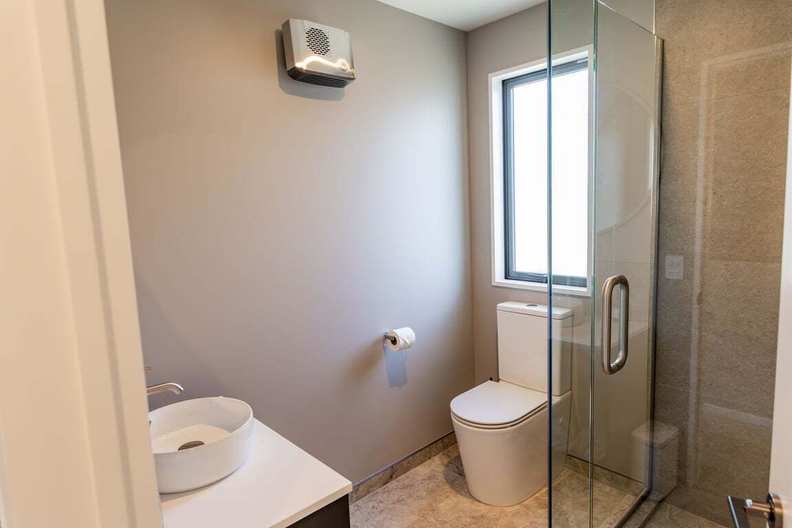 A bathroom with a toilet, a glass shower enclosure, a toilet paper holder, and a window providing natural light.
