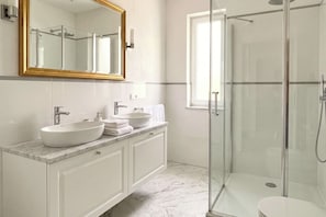 Ein modernes Badezimmer mit einer Duschkabine aus Glas, einem großen Spiegel und einer Marmorarbeitsplatte.