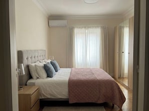 A bedroom with a bed, bedside table, lamp, and a window with curtains. - Alfama Pearl Apartment by Agsuites com (Lisboa)