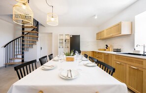 A dining area with a white table set for four, black chairs, a staircase with wooden steps, and a kitchen with wooden cabinets and a black refrigerator. - Gorgeous home in Kornati with WiFi (Kornati)