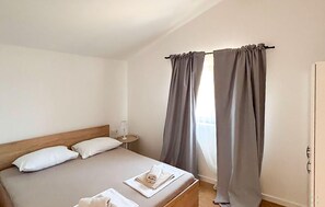 Een slaapkamer met een bed, kussens, een nachtkastje en gordijnen.