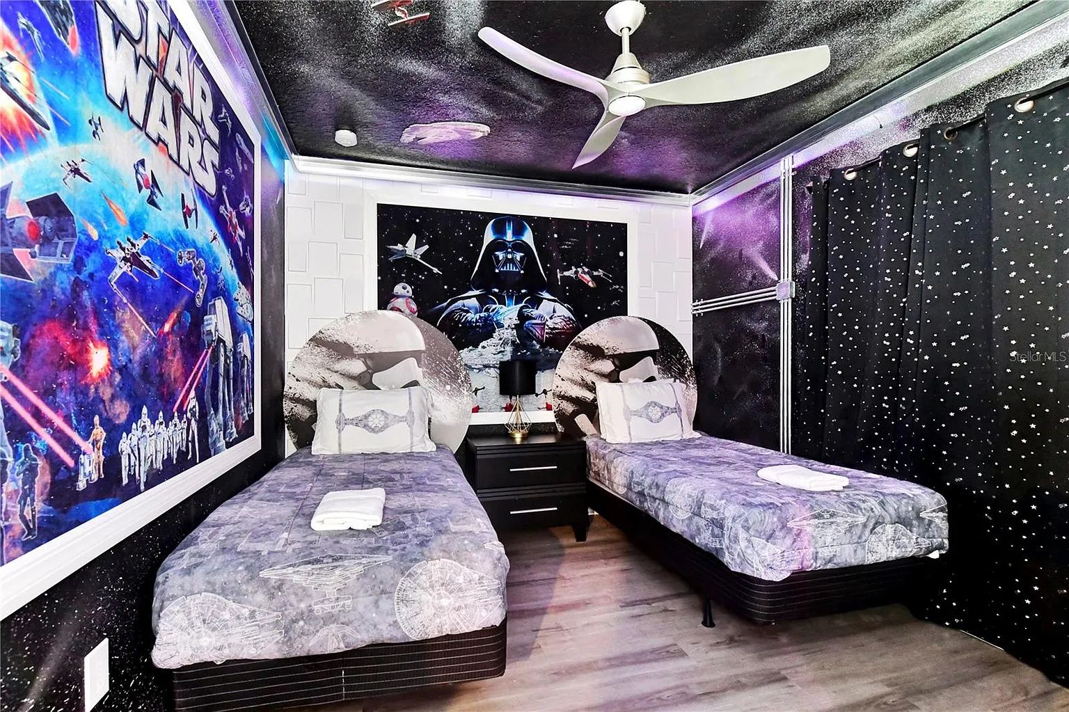 Un dormitorio con temática de Star Wars, que presenta un mural grande, dos camas, un ventilador de techo y una pared con estrellas.