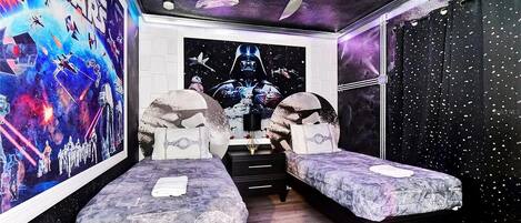 Un dormitorio con temática de Star Wars, que presenta un mural grande, dos camas, un ventilador de techo y una pared con estrellas.