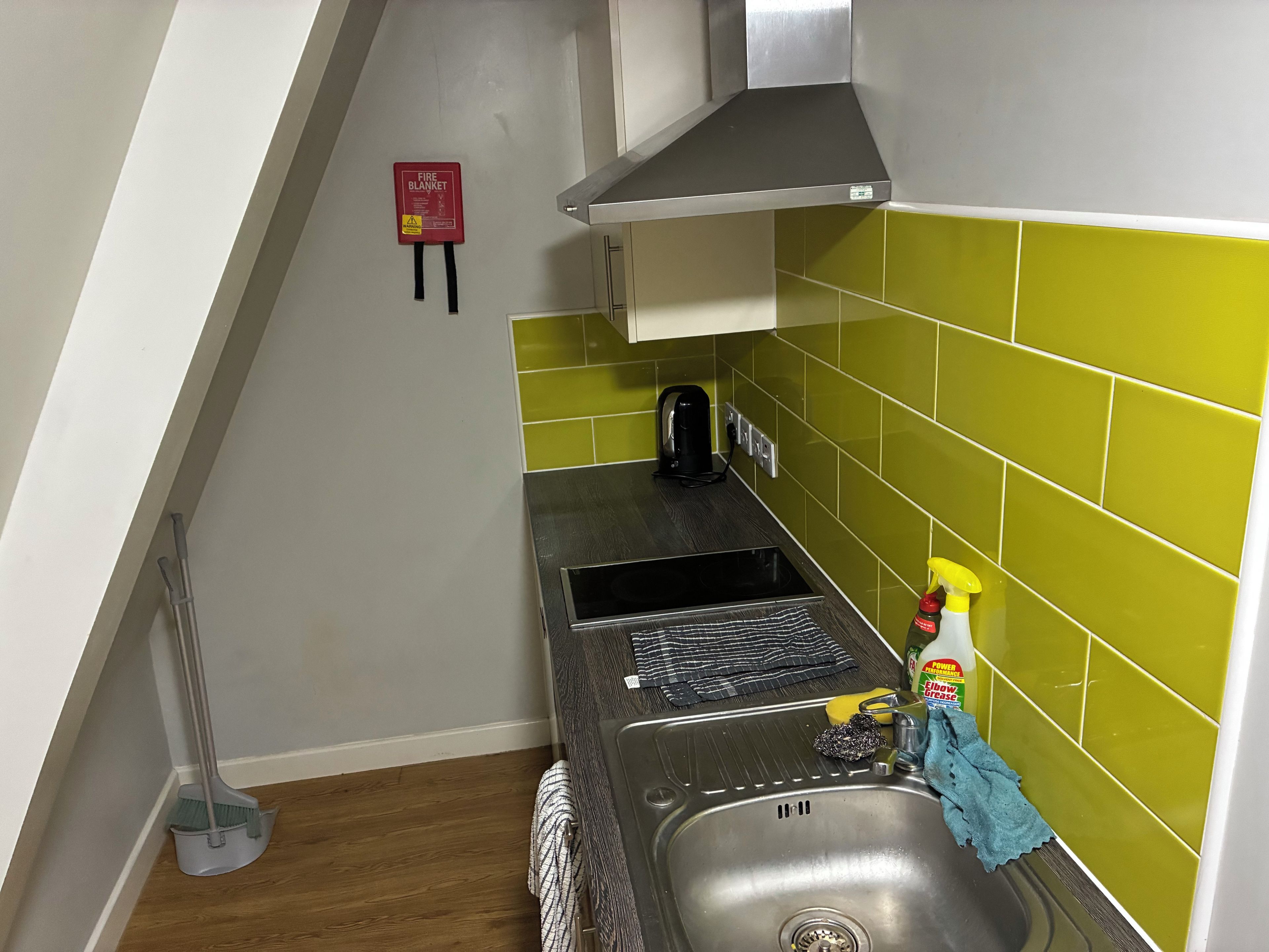 A kitchen with a sink, a fire blanket, a kettle, and a cleaning spray.