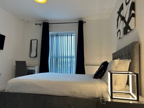 Ein modernes Schlafzimmer mit einem großen Bett, einem Schreibtisch und einem Fenster mit Vorhängen.
