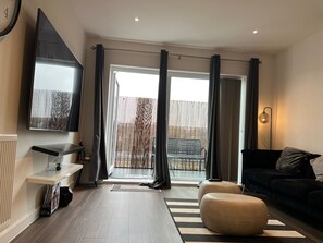 Ein modernes Wohnzimmer mit Fernseher, einer Couch, einem Couchtisch und einer Glastür zum Außenbereich.