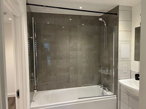 Ein modernes Badezimmer mit einer Glaskabine zur Dusche, einer weißen Badewanne und einem großen Spiegel über dem Waschbecken.
