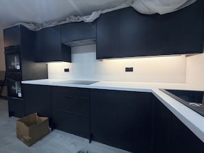 A modern kitchen with dark cabinetry, a white countertop, and under-cabinet lighting. - House Sleeps 6 with Patio (Cardiff)