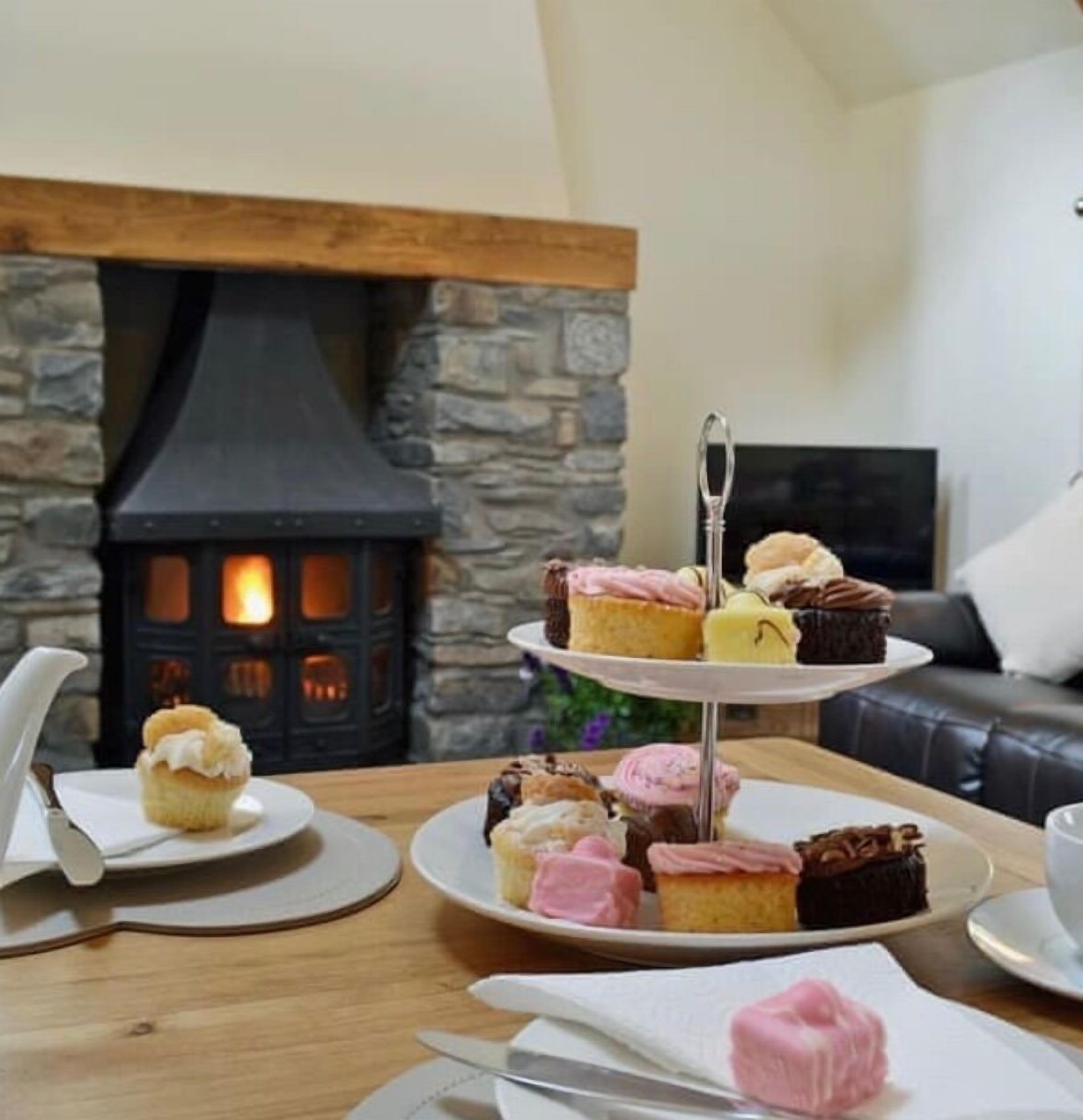 Una mesa de comedor con un soporte de tres niveles para postres, una chimenea y un televisor al fondo.