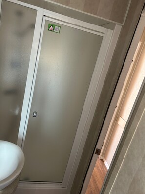 A bathroom with a toilet, a door with a warning sign, and a partially visible shower area. - Cabin Sleeps 8 with Sea Views and Parking (Morecambe)
