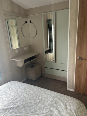 A bedroom with a bed, a bedside table, a mirror, a wardrobe, and a door.