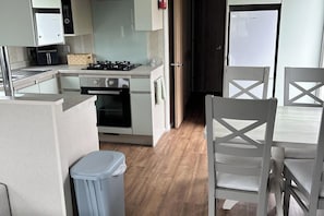 A compact kitchen with a stove, oven, and microwave, a trash bin, and a dining area with a table and chairs.