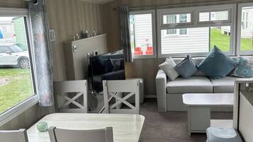 A compact room with a sofa, a television, a dining table, and a window with a view of a vehicle and a building outside.