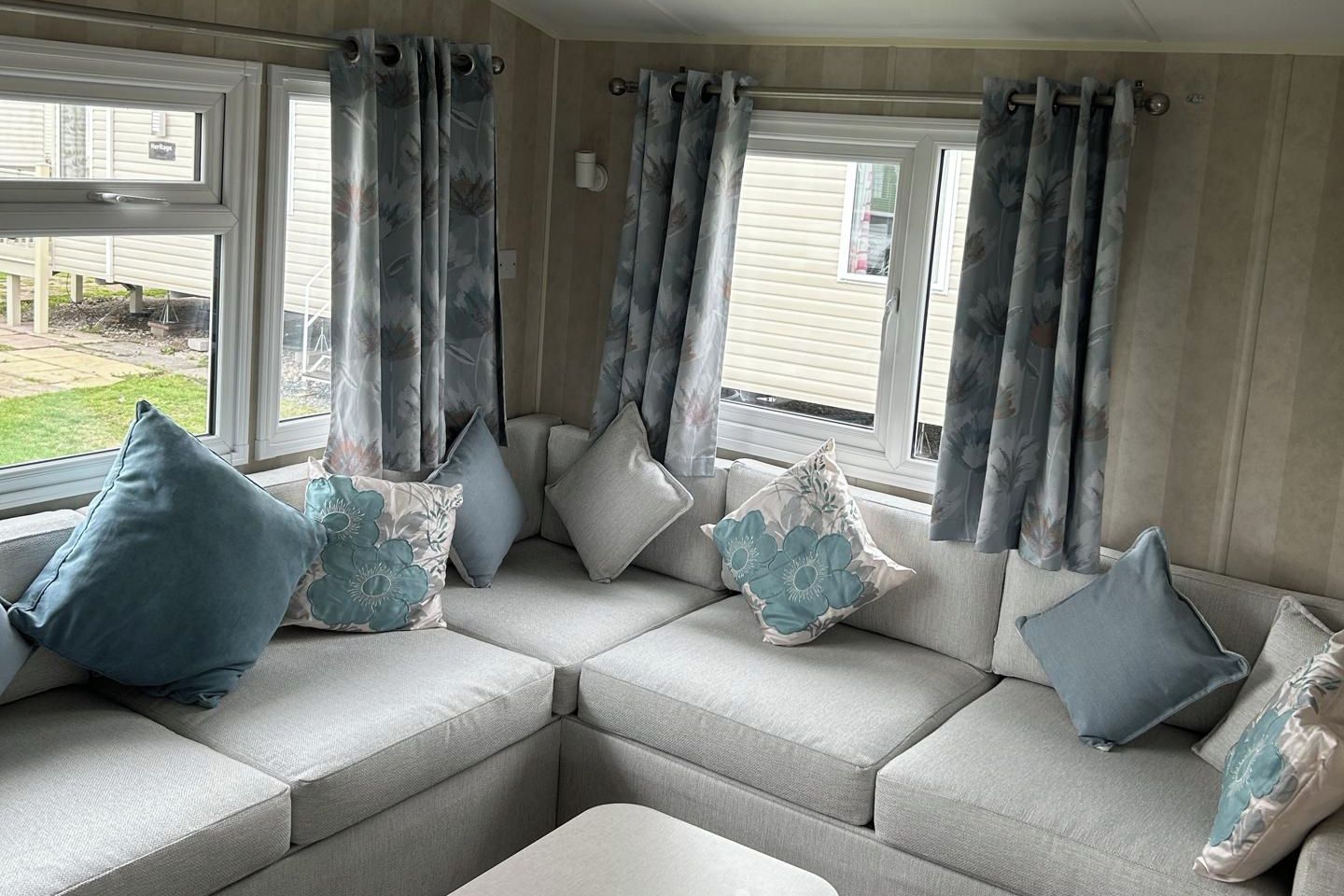 A cozy seating area with a sectional sofa, floral cushions, and a view of the outdoors through large windows.