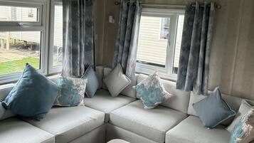 A cozy seating area with a sectional sofa, floral cushions, and a view of the outdoors through large windows.