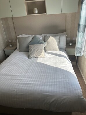 A neatly made bed with a striped bedspread, a headboard with built-in shelves, and bedside tables with lamps and decorative items. - Cabin Sleeps 8 with Sea Views and Parking (Morecambe)