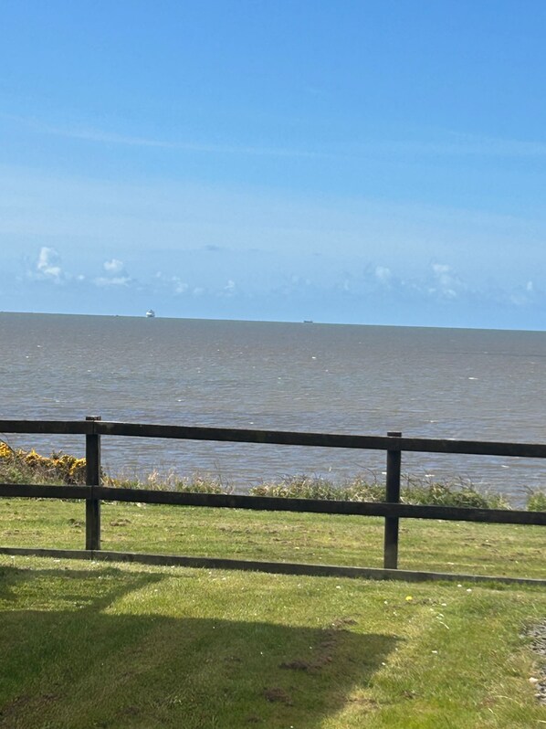 A grassy area with a metal railing in the foreground, leading to a body of water. - Cabin Sleeps 8 with Sea Views and Parking (Morecambe)