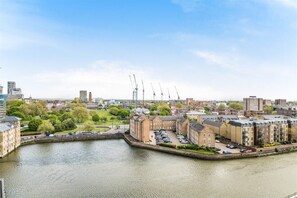 A riverside view of a city with buildings, a dock, and cranes in the distance. - Cosy Barking Apartment with City Views (Barking)