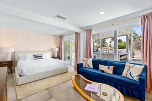Ein modernes Hotelzimmer mit Bett, blauem Sofa, Glastisch und Blick ins Freie.