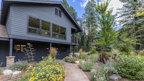 Une maison moderne à deux étages, dotée d’un porche couvert et entourée d’un jardin aménagé avec diverses plantes et fleurs.