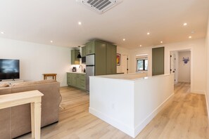 A modern kitchen with green cabinets, a central island, and a dining area with a sofa and table.