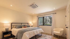 Une chambre à coucher avec un lit, des lampes de chevet, une fenêtre avec des rideaux, une chaise et un tapis à motifs.
