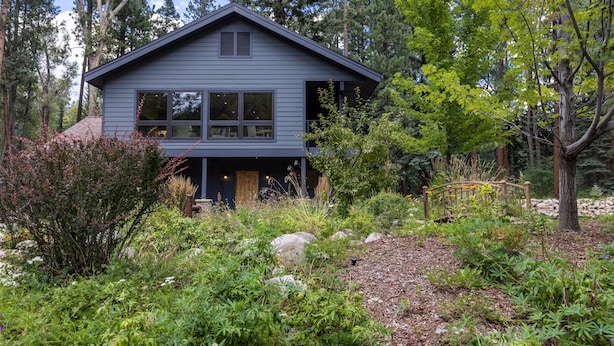 Une maison à deux étages, à l’extérieur sombre, entourée d’un paysage naturel composé d’arbres et d’arbustes.
